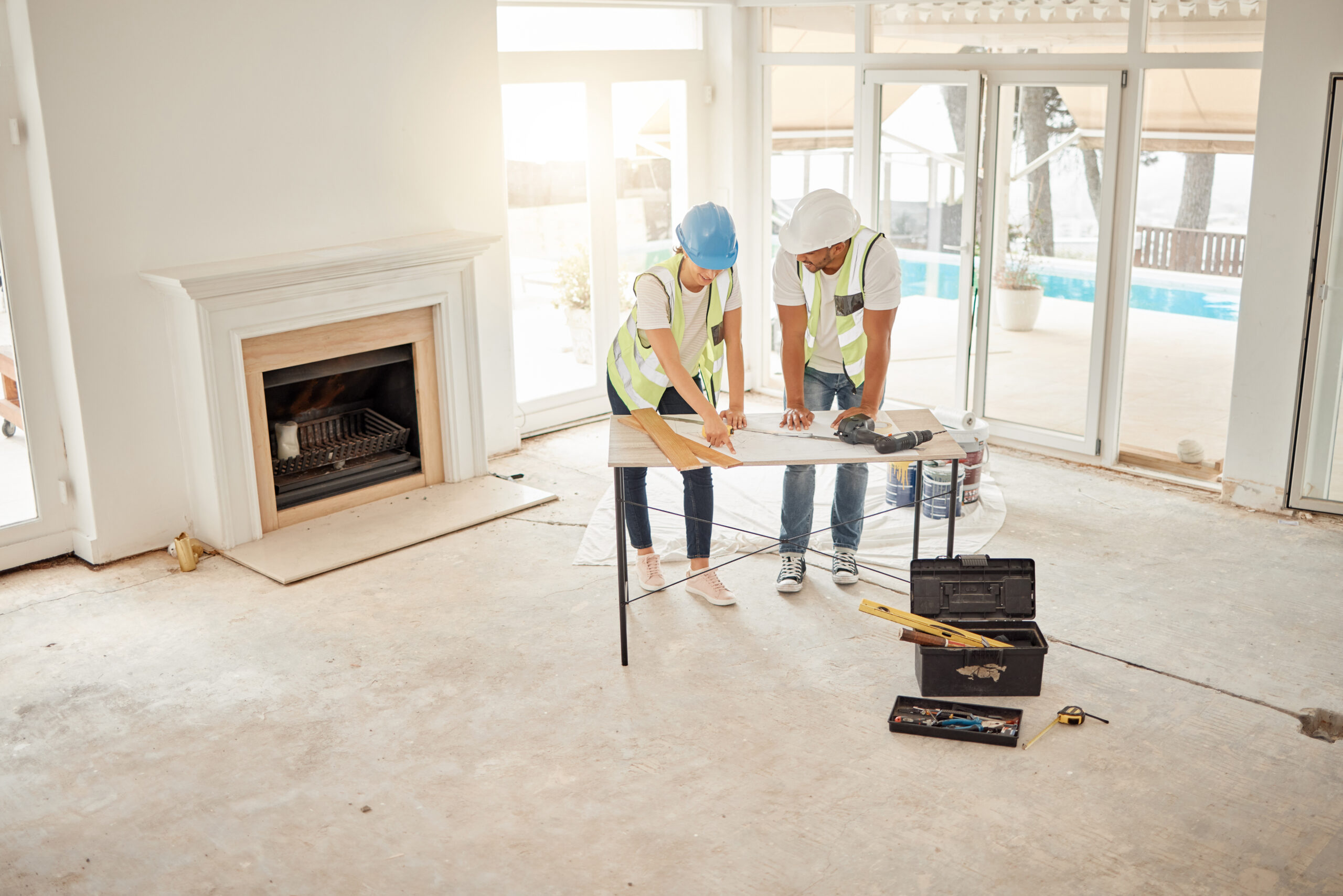 Two workers wearing safety vests and helmets looking at a blueprint