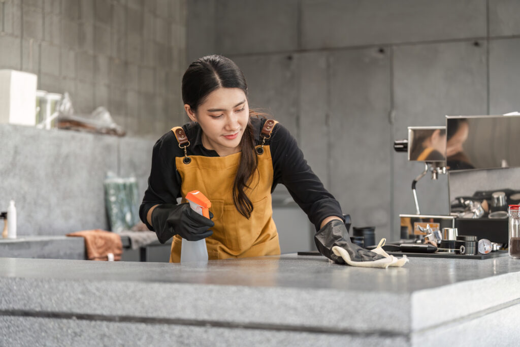 A female barista cleaning a coffee countertop using spray and cloth.