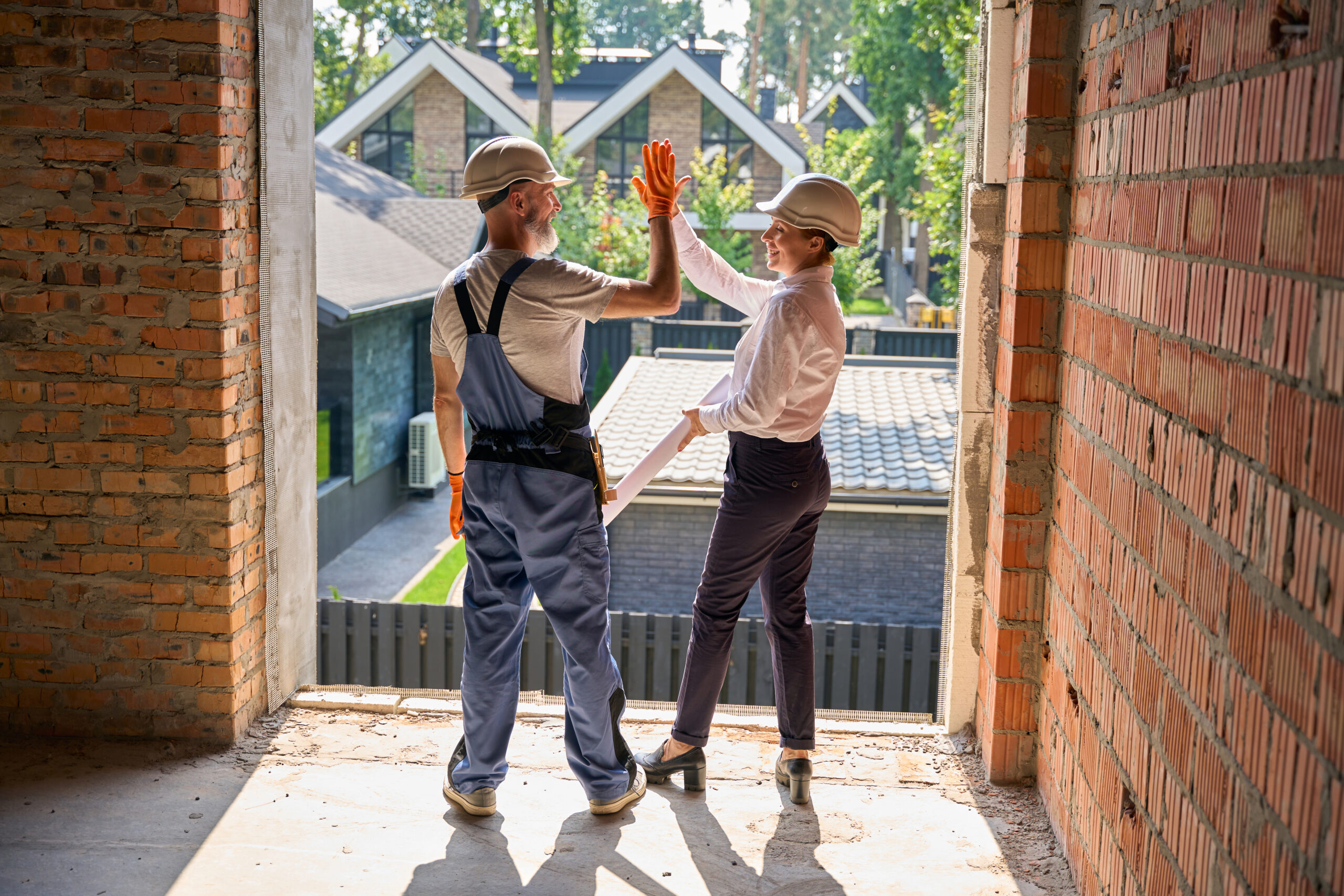 Two construction supervisors giving high fives to each other after a successful home restoration project.