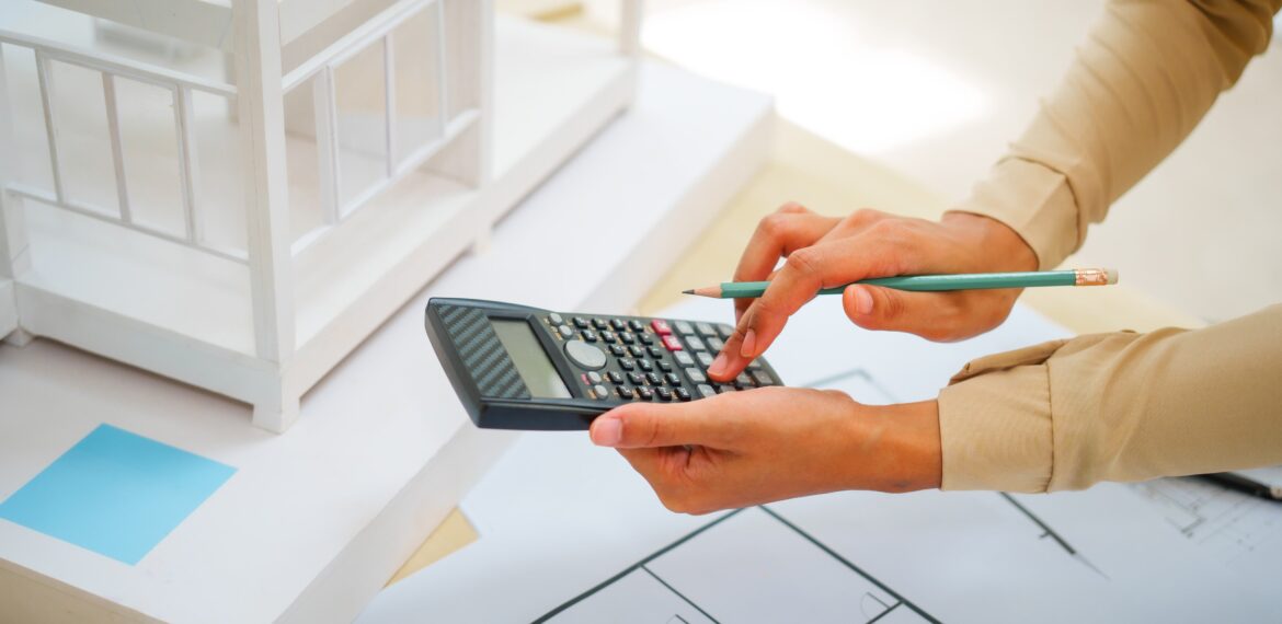 A close-up shot of an architect's hands using a calculator while analyzing a house design blueprint.