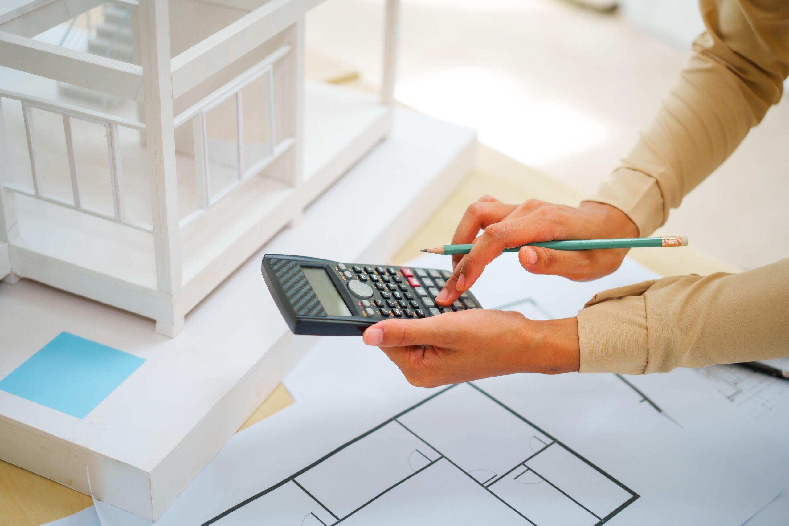 A close-up shot of an architect's hands using a calculator while analyzing a house design blueprint.