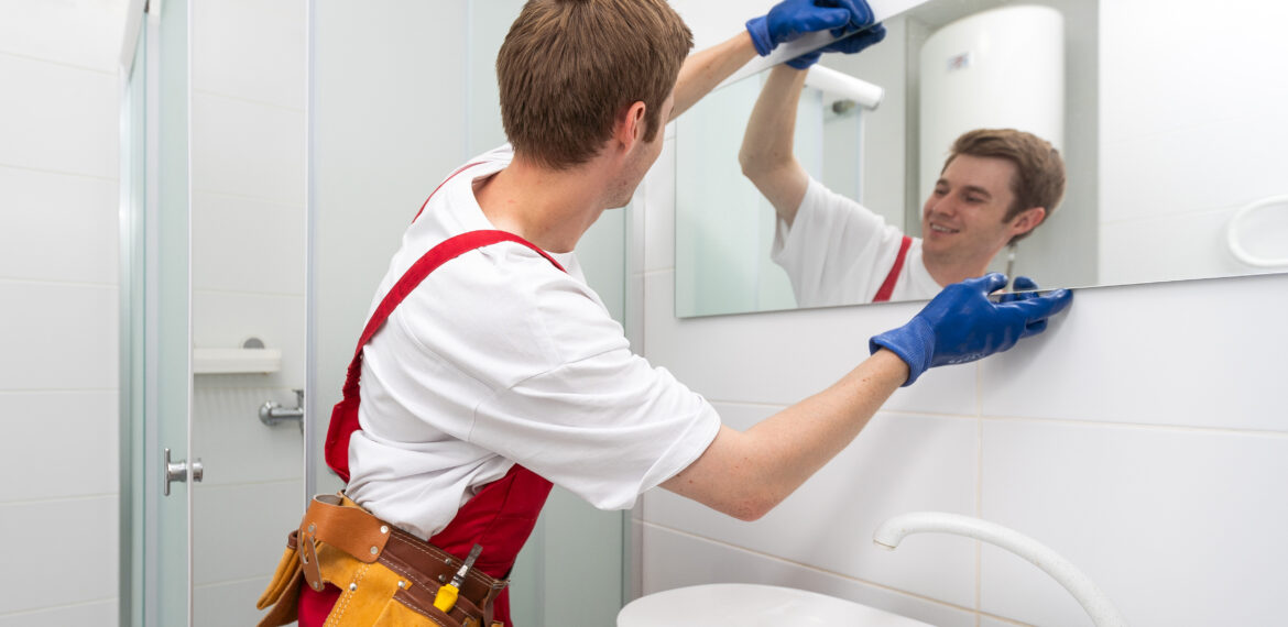 A male carpenter is installing a mirror on the bathroom wall.