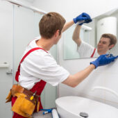 A male carpenter is installing a mirror on the bathroom wall.