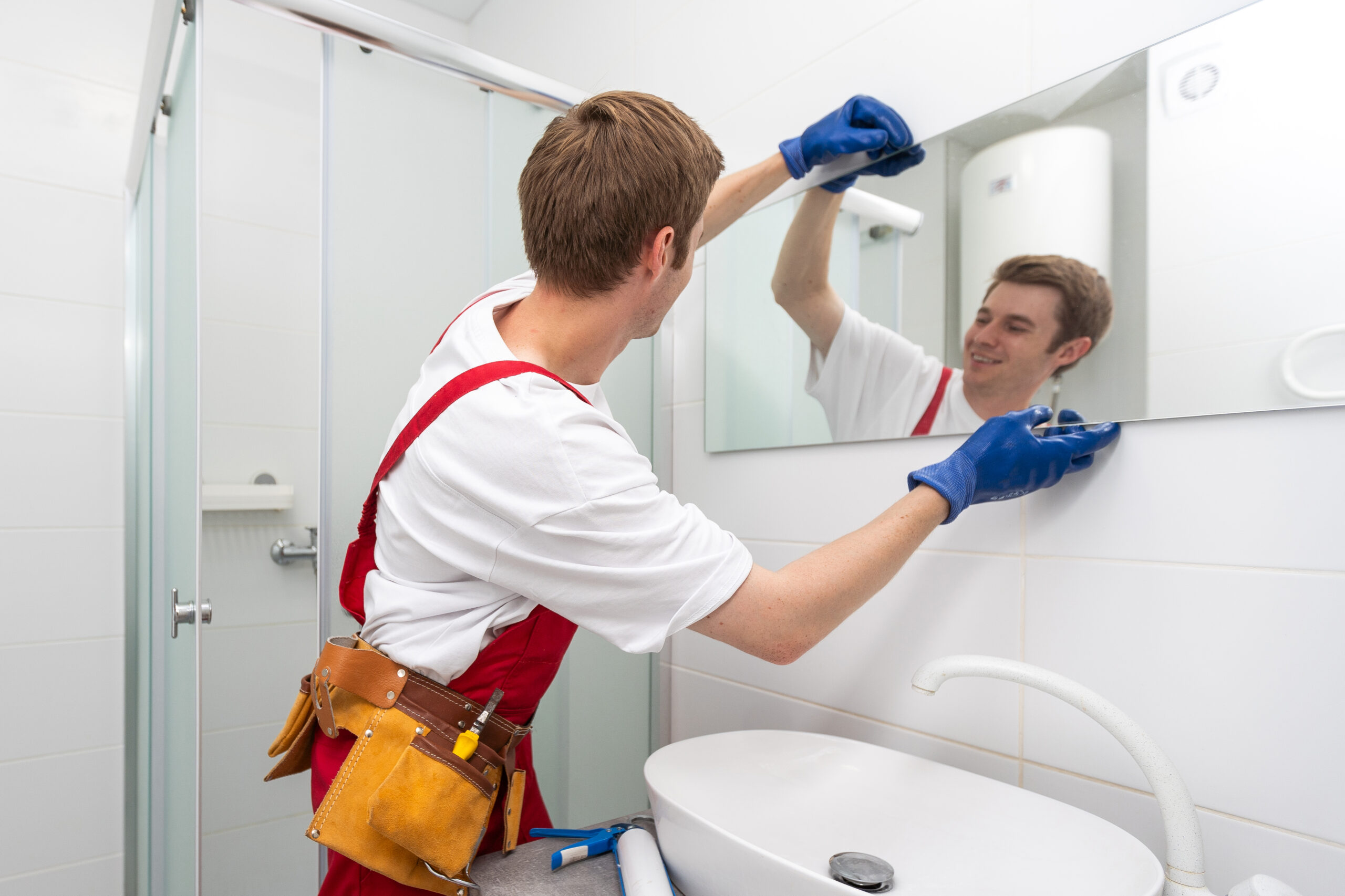 A male carpenter is installing a mirror on the bathroom wall.