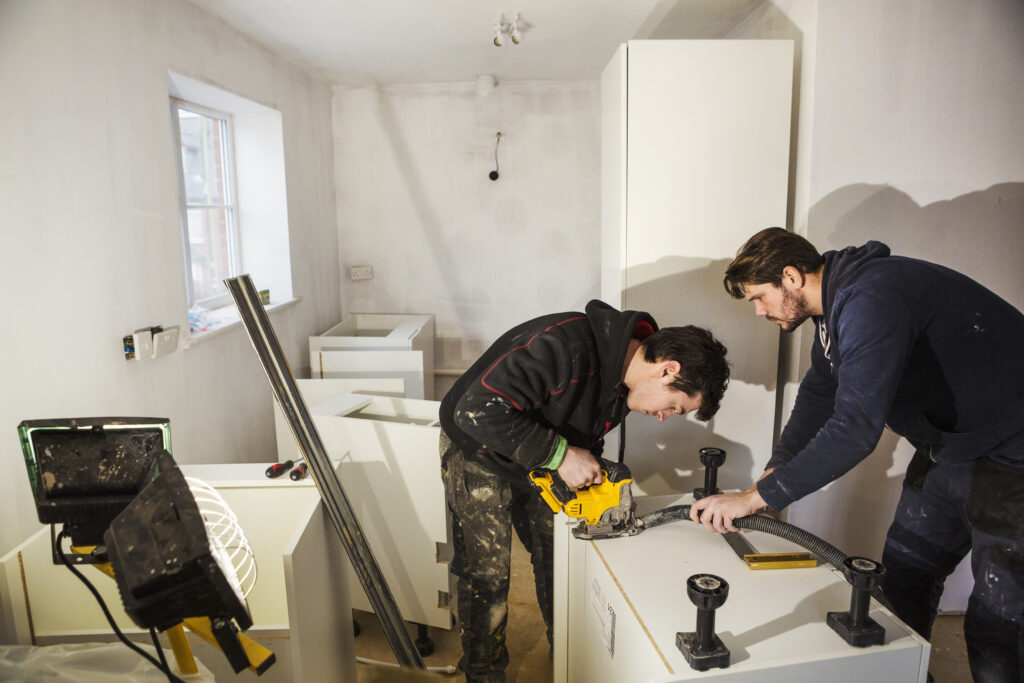 Two builders cutting plasterboards for a kitchen unit.