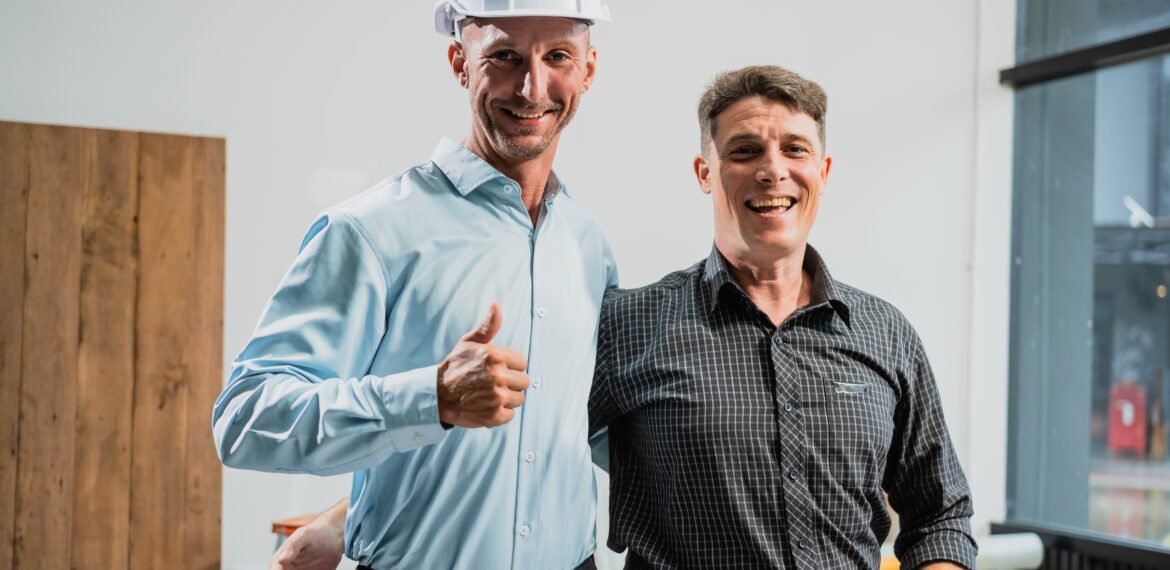 A home remodeler wearing a hard hat smiles at the camera along with a male client.