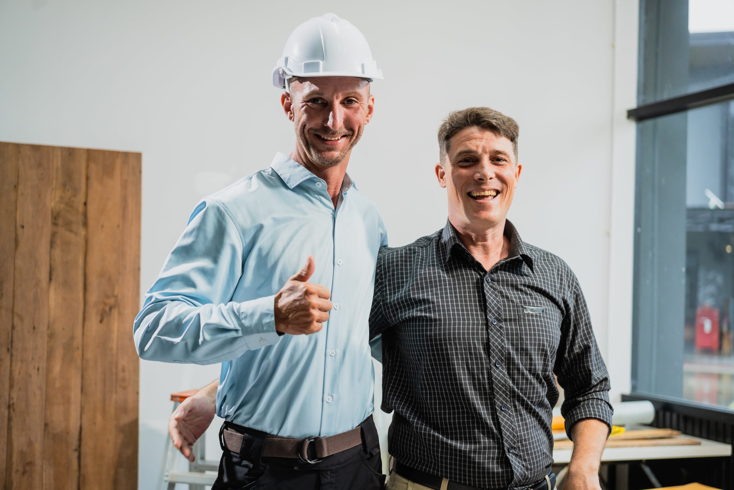 A home remodeler wearing a hard hat smiles at the camera along with a male client.